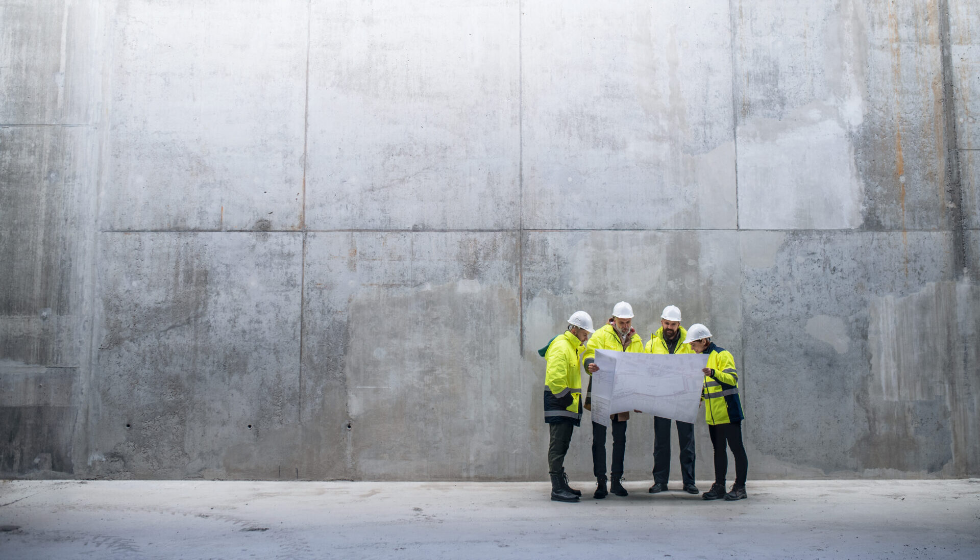 A group of engineers standing against concrete wall on construction site.